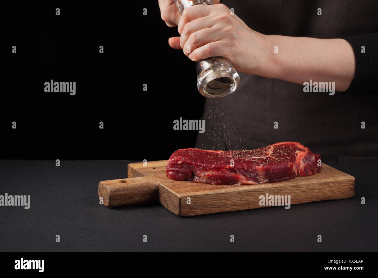 Une femme cuisine avec des poivrons steak de boeuf marbré sur un fond sombre. Arrière-plan de l'alimentation. Zone de texte noir. Copier l'espace. Banque D'Images Une femme cuisine avec des poivrons steak de boeuf marbré sur un fond sombre. Arrière-plan de l'alimentation. Zone de texte noir. Copier l'espace. Banque D'Images