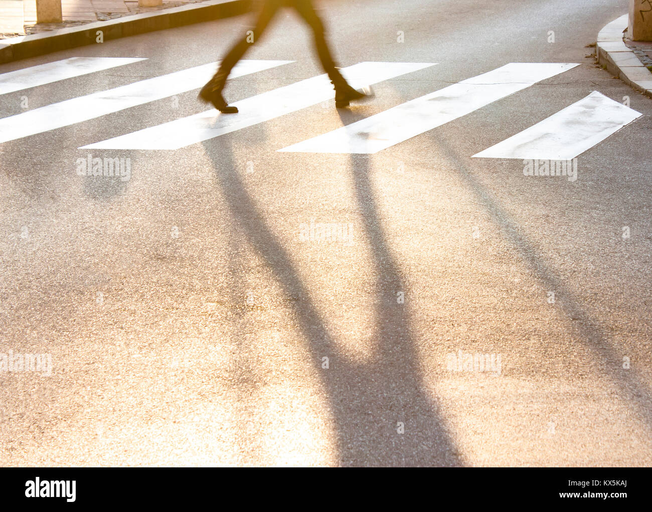 Les jambes et l'ombre floue d'une adolescente de traverser la petite rue de la ville au coucher du soleil dans une hâte Banque D'Images