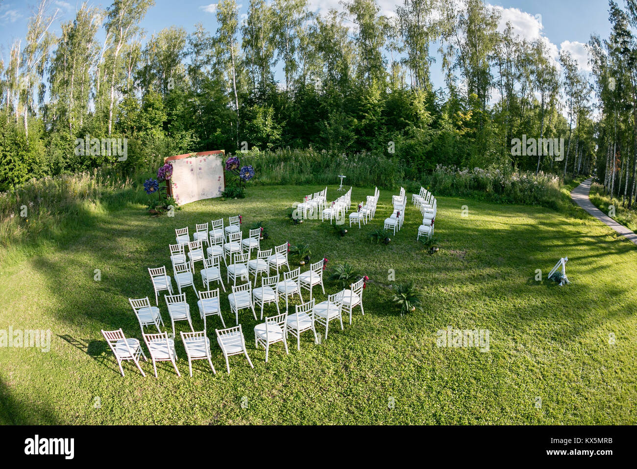 Cadre magnifique pour la cérémonie de mariage en plein air attendent les mariés et les invités. Chaises blanches décorées de fleurs, sont dans la zone de la cérémonie de mariage dans une forêt Banque D'Images
