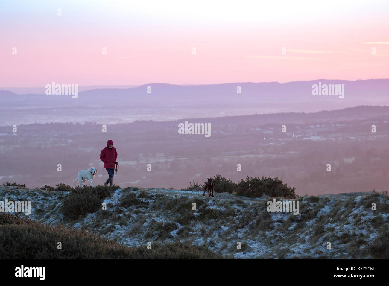 Flintshire, Pays de Galles, Royaume-Uni. 8 janvier, 2018. Météo France : Une autre nuit claire pour beaucoup et une fois de plus répandue des températures de gel. Un marcheur avec deux chiens walkign le long d'un sentier pour les contours de l'âge du fer de Fortin Moel-y-Gaer sur la montagne Halkyn dans Flintshire comme le soleil se brise l'horizon et les inondations le beau paysage avec Crédit : couleur/DGDImages Alamy Live News Banque D'Images