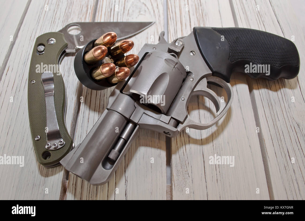 Un couteau pliant ouvert avec une poignée verte ainsi qu'une vitesse de chargement loader et un revolver en acier inoxydable placé sur une table en bois blanc Banque D'Images