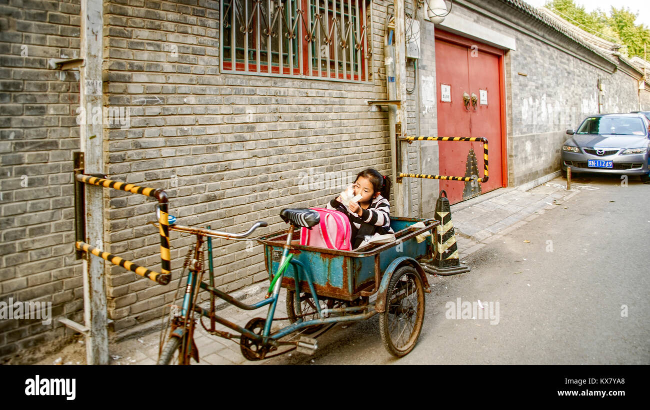 Une jeune fille se trouve dans un panier de vélo dans la place de stationnement réservée à sa résidence. Houton traditionnel salon. Beijing, Chine Banque D'Images