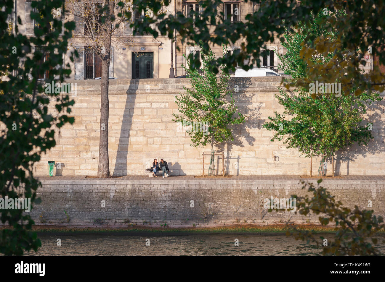 Jeunes divers Paris, vue d'un couple assis ensemble au soleil le long du quai d'Orléans sur l'Ile St Louis dans le centre de Paris, France. Banque D'Images