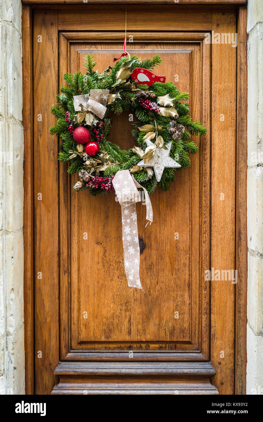 Vue frontale d'une couronne de Noël traditionnel fait de branches d'arbre de pin rouge, des boules de Noël et houx Feuilles et baies accrochées sur une porte en bois. Banque D'Images