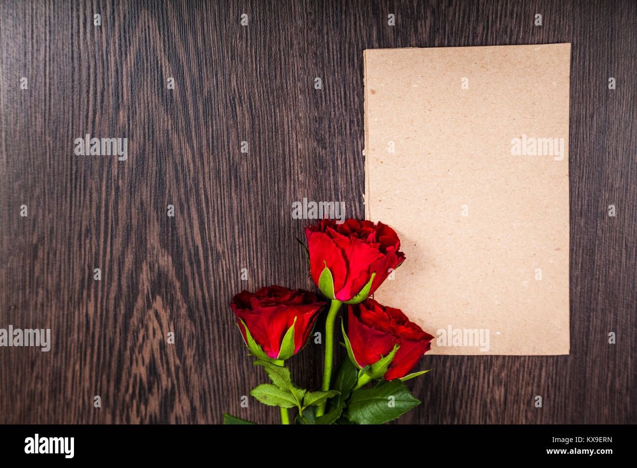Roses rouges et carte sur un fond de bois. Carte de souhaits avec la Saint-Valentin, anniversaire ou mariage. Banque D'Images Roses rouges et carte sur un fond de bois. Carte de souhaits avec la Saint-Valentin, anniversaire ou mariage. Banque D'Images