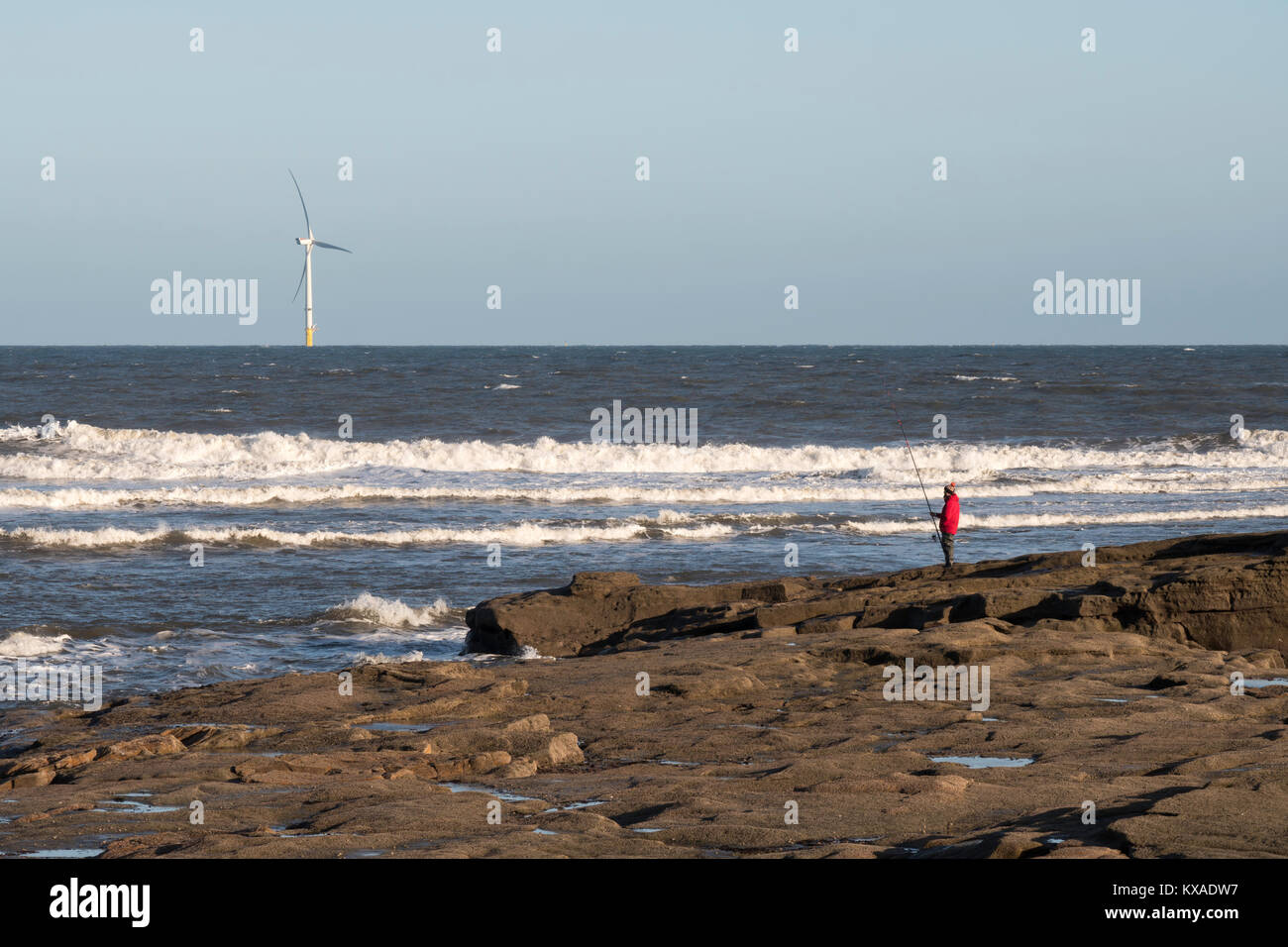 Un pêcheur à la pêche à la ligne avec la tige et juste au nord de Seaton Sluice, avec une éolienne à l'arrière-plan, Northumberland, England, UK Banque D'Images