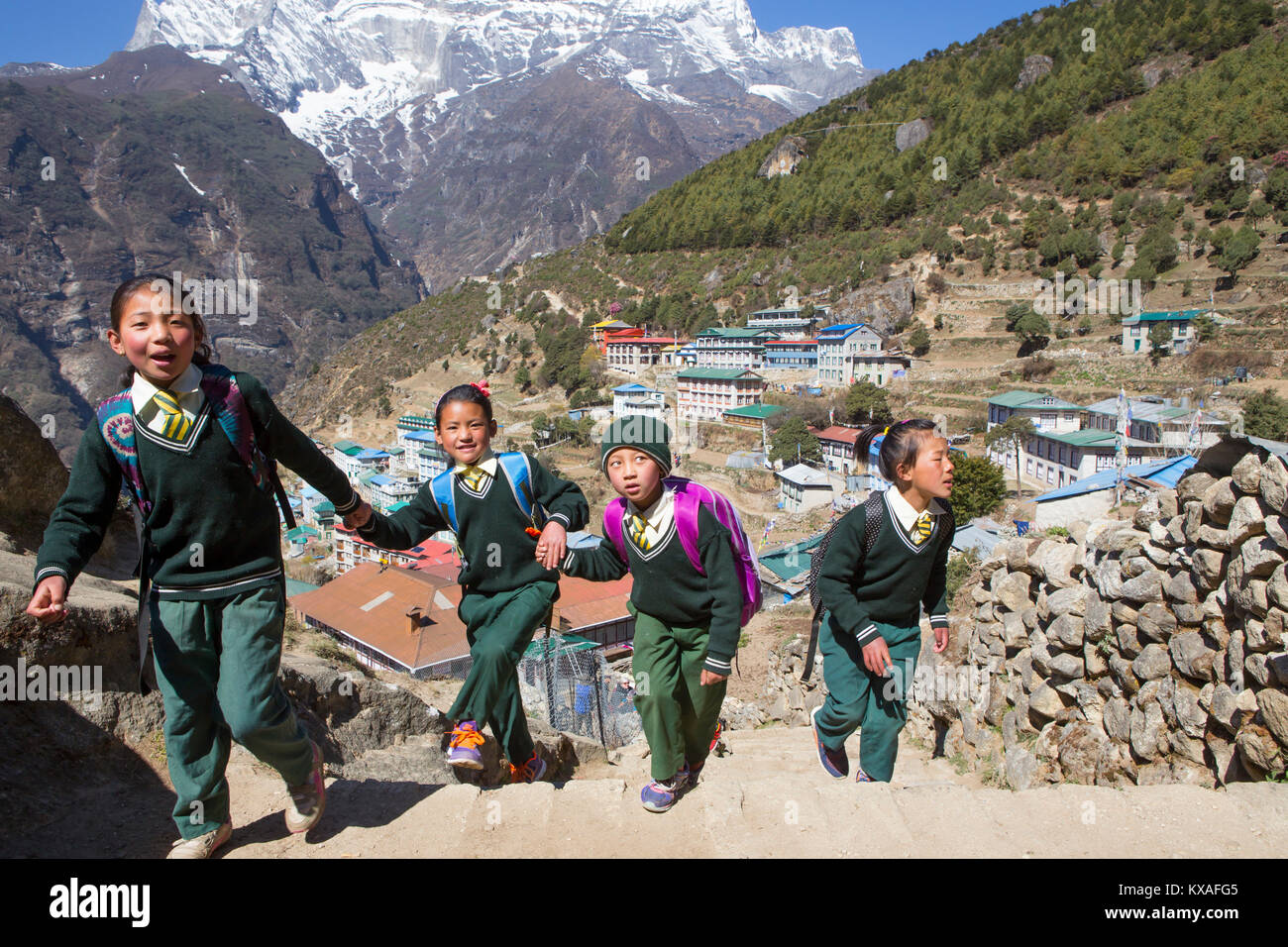 Quatre jeunes enfants vêtus de l'uniforme est la marche en montagne Namche Bazar, un village de montagne dans la vallée du Khumbu au Népal. Banque D'Images