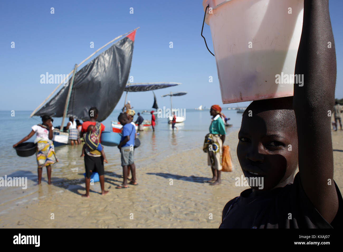 Personnes porteuses de bols et seaux en face de voiliers en attente sur plage côtière, au Mozambique Banque D'Images