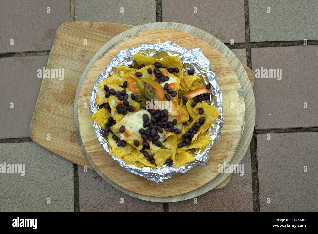 Nachos mexicains ou d'Amérique latine - Close up d'haricots noirs piment jalapeno sur tortillas de maïs au fromage fondu sur le plateau en bois. Banque D'Images