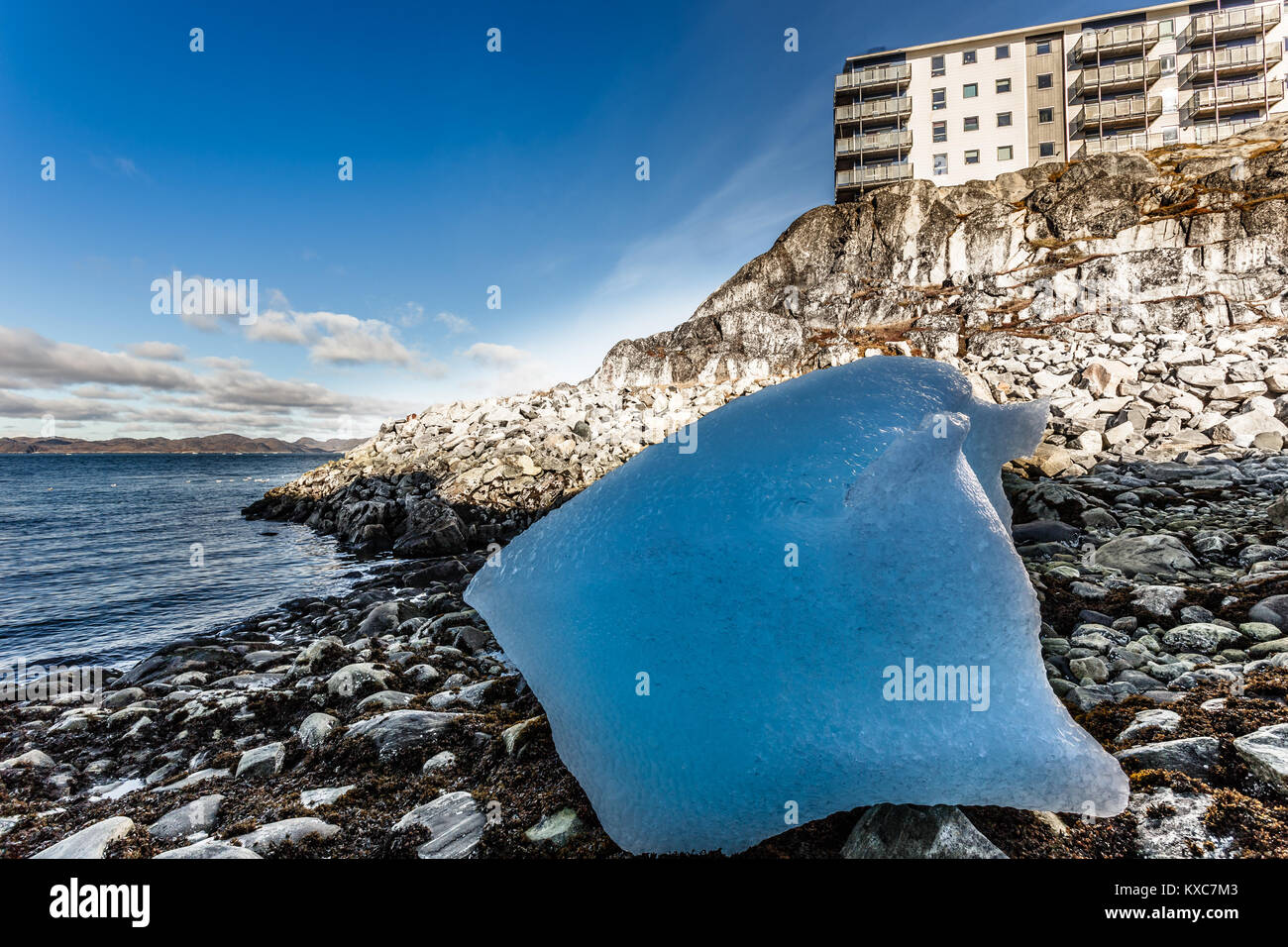 Gros morceau de glace bleue portant parmi les pierres sur la rive avec les Inuit moderne établi sur la colline au fjord, Nuuk, Groenland ville Banque D'Images