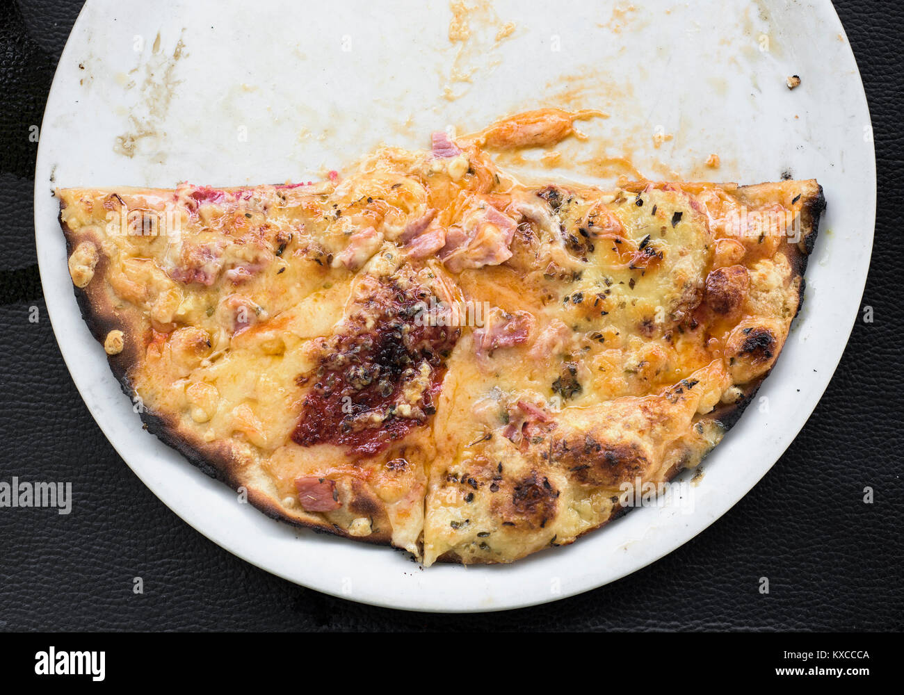D'un grand angle de vue d'une plaque en céramique blanc avec la moitié de la pizza, sur une surface en similicuir noir Banque D'Images