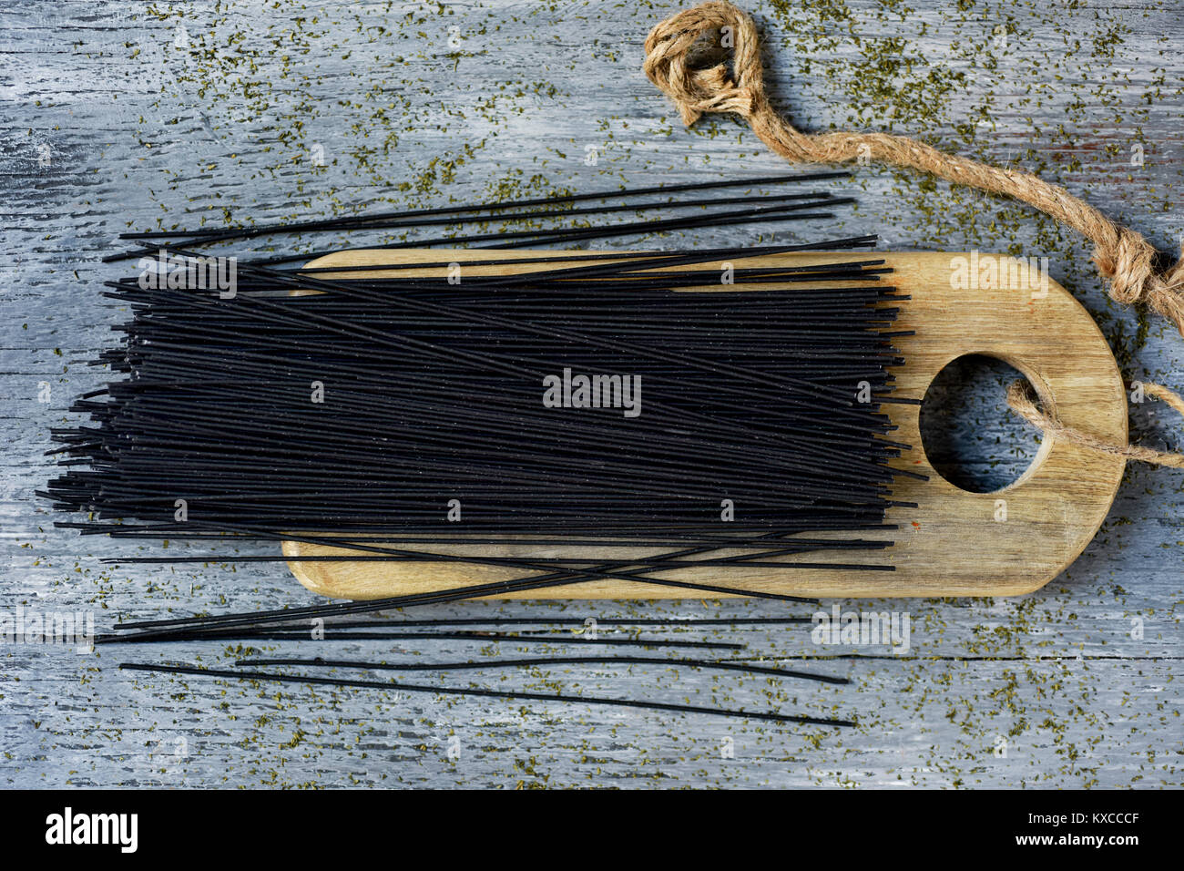 Portrait d'un tas de spaghetti noir non cuit sur une planche à découper en bois, placé sur une table en bois rustique gris Banque D'Images