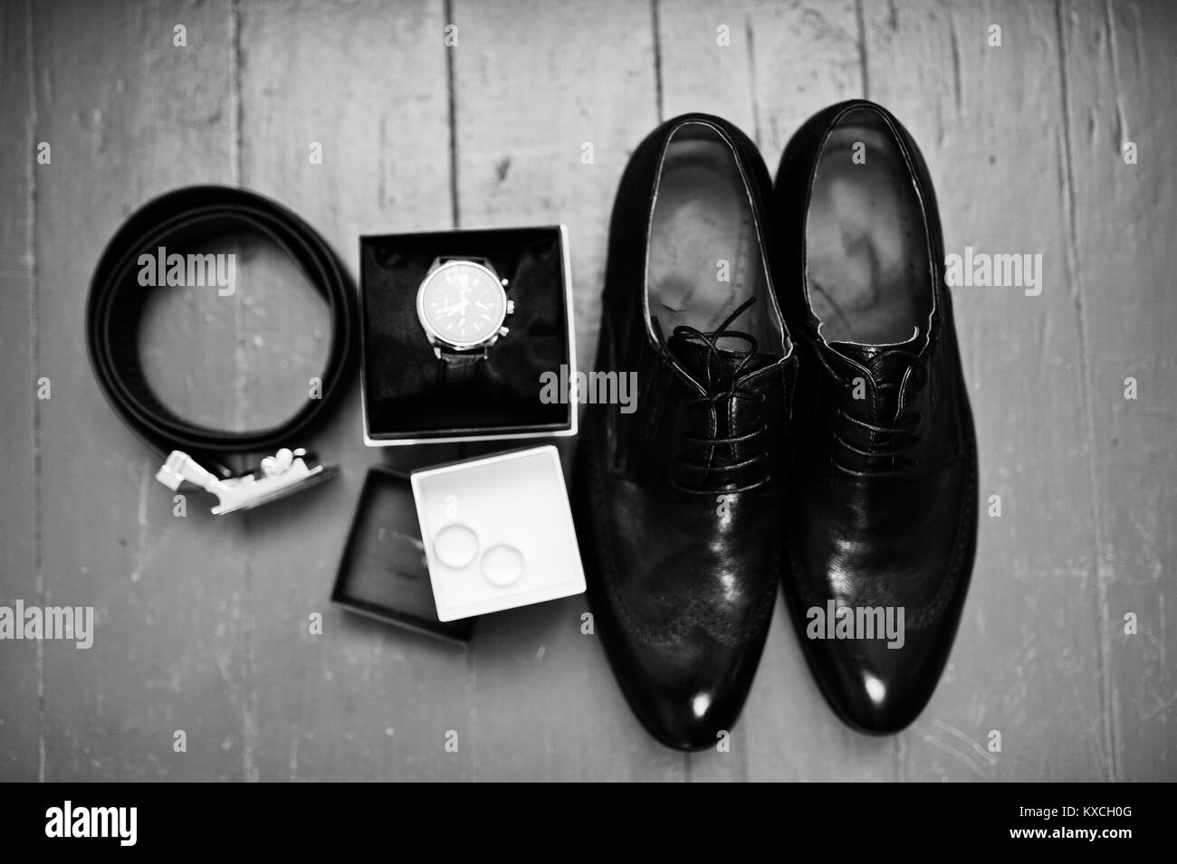 Photo en gros plan des chaussures du marié noir brogue, regarder, les anneaux de mariage, ceinture et noeud papillon sur le fond en bois. Photo en noir et blanc. Banque D'Images