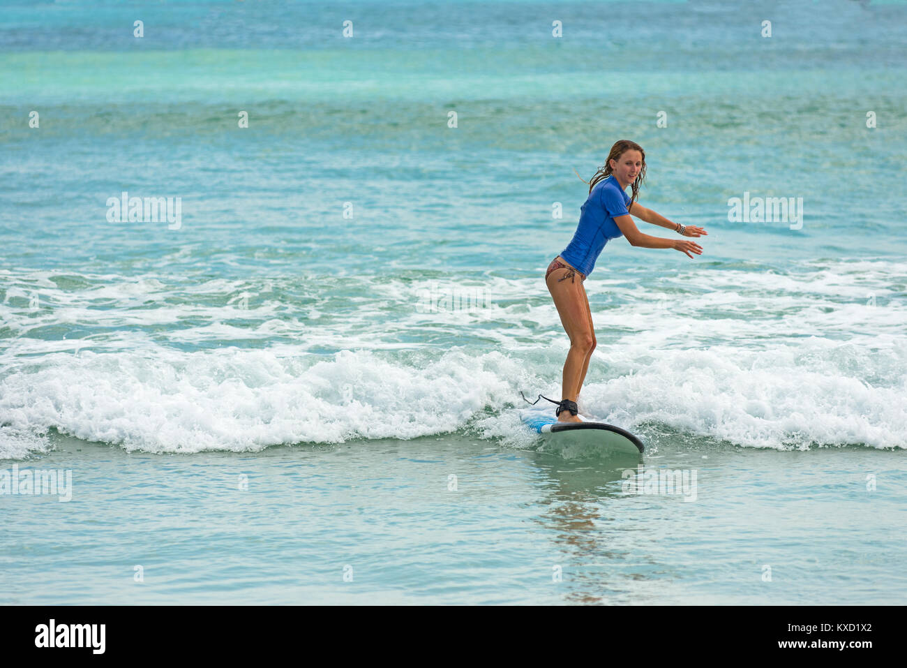 Jeune femme apprend à surfer sur un long board sur les vagues de l'apprenant dans un endroit paradisiaque. Banque D'Images