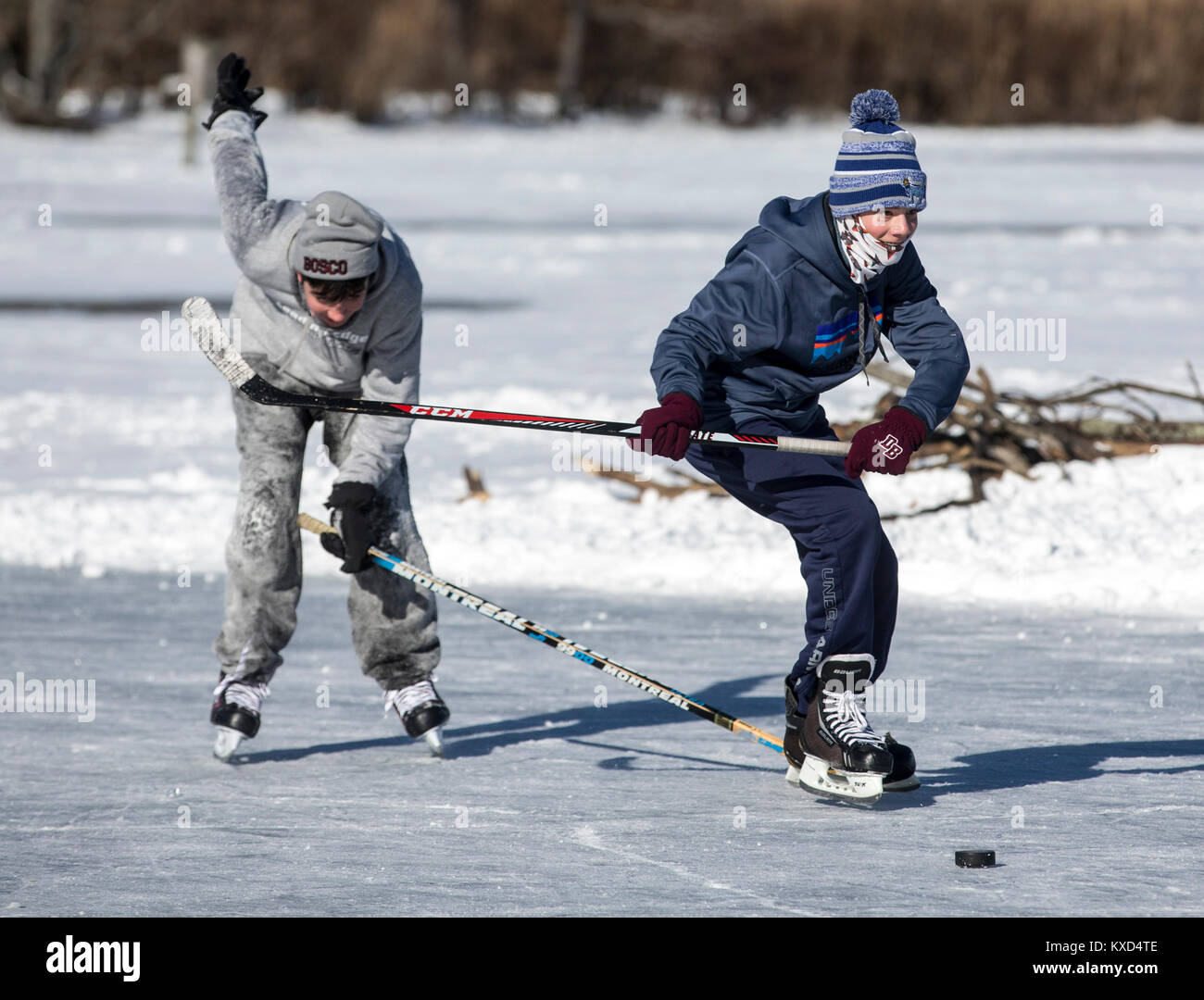 Garçons jouant au hockey sur glace sur un étang gelé par temps froid Banque D'Images