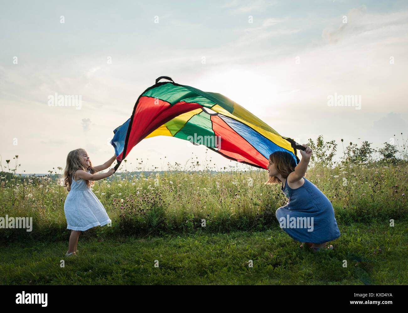 Sœurs espiègles jouant avec des textiles colorés on grassy field against sky Banque D'Images