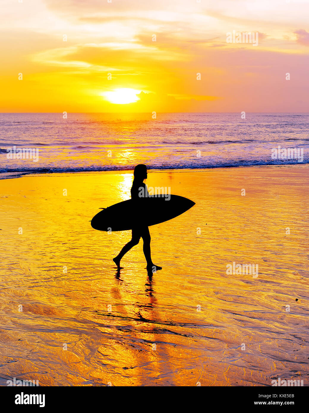 Surfeur femme marchant sur la plage avec une planche de surf au coucher du soleil. L'île de Bali Banque D'Images