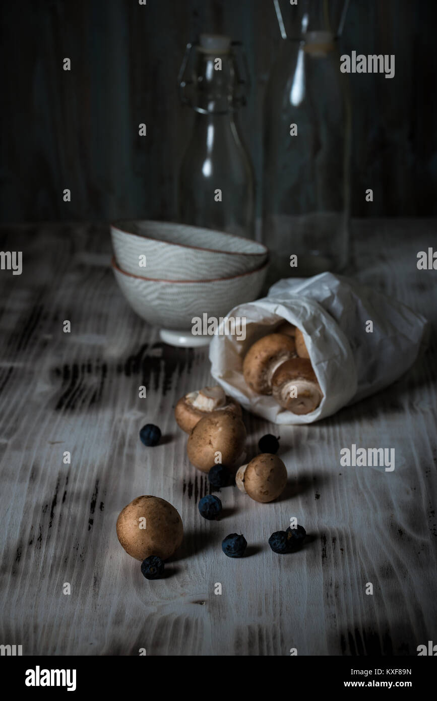 Photo verticale de plusieurs champignons comestibles brun avec bouchon. Champignons renversé sur vintage wooden board à partir de sac de papier avec quelques fruits secs. Deux bols Banque D'Images