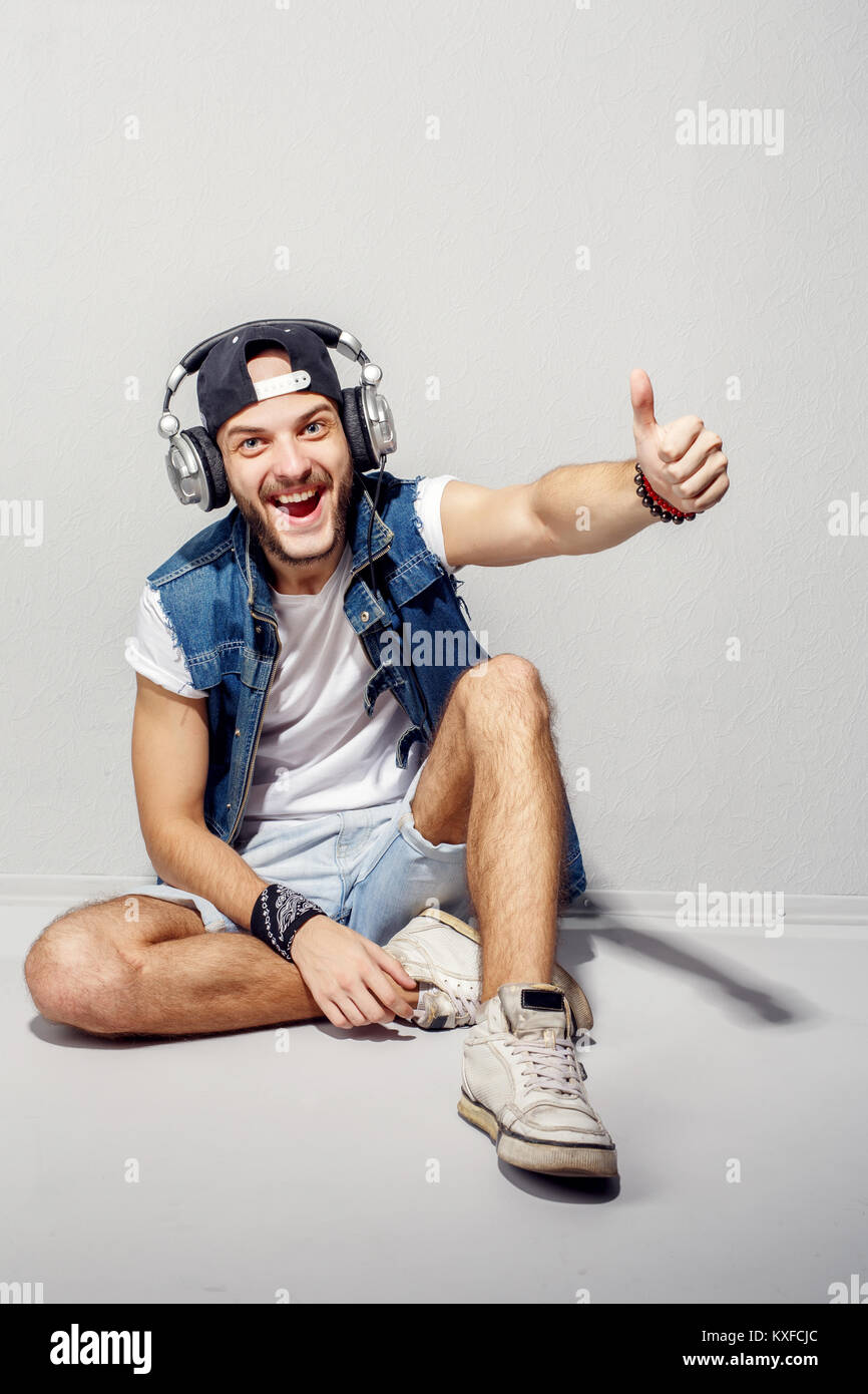 Dans le rythme de ma musique. Ambiance jeune homme barbu dans les écouteurs assis près de mur gris et l'écoute de la musique. Banque D'Images