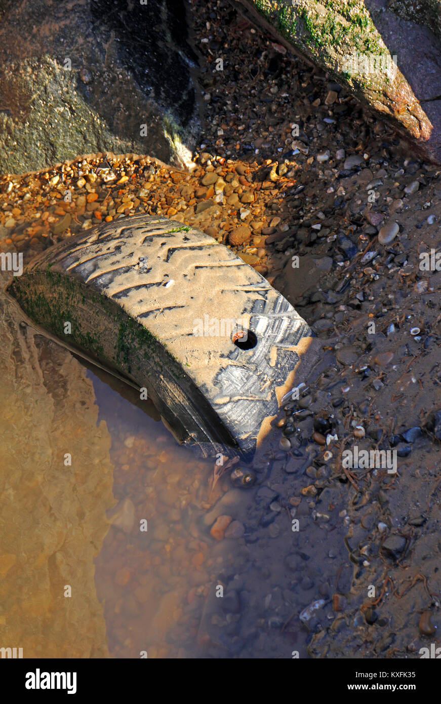 Un vieux pneu abandonné à moitié enfoui sur une plage à Norfolk, Angleterre, Royaume-Uni. Banque D'Images