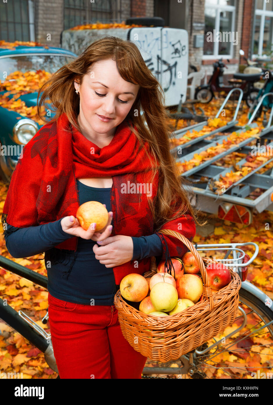 Jolie fille avec panier de pommes et un vélo dans la cour couverte de feuilles d'automne Banque D'Images