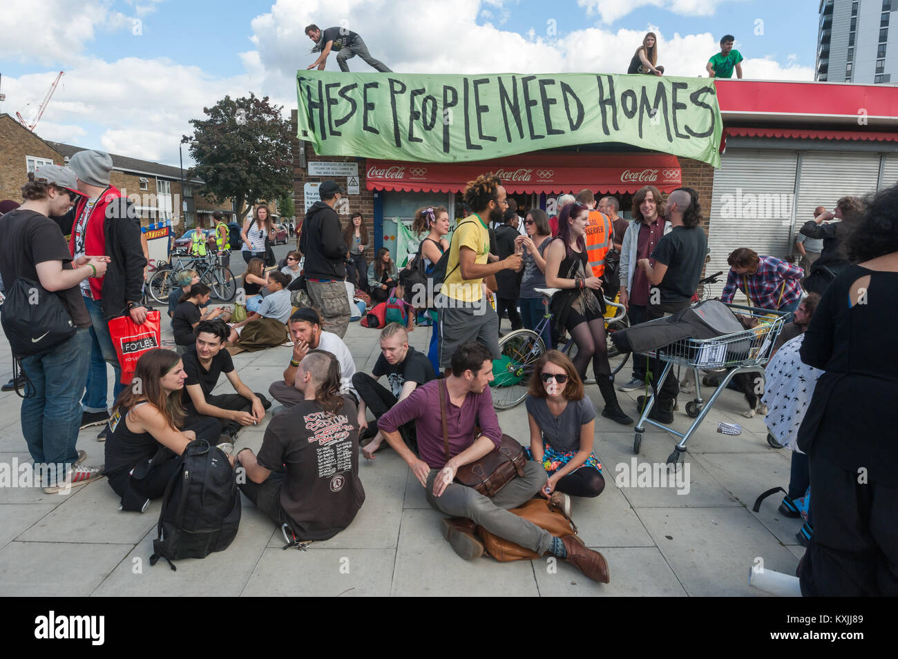 Les gens s'assoient devant les magasins sur les charpentiers Estate, Stratford comme gens abandonnent le Focus E15 banner 'ces gens ont besoin depuis le toit des maisons au cours de la célébration de deux années de protestation par logement Focus E15. Banque D'Images