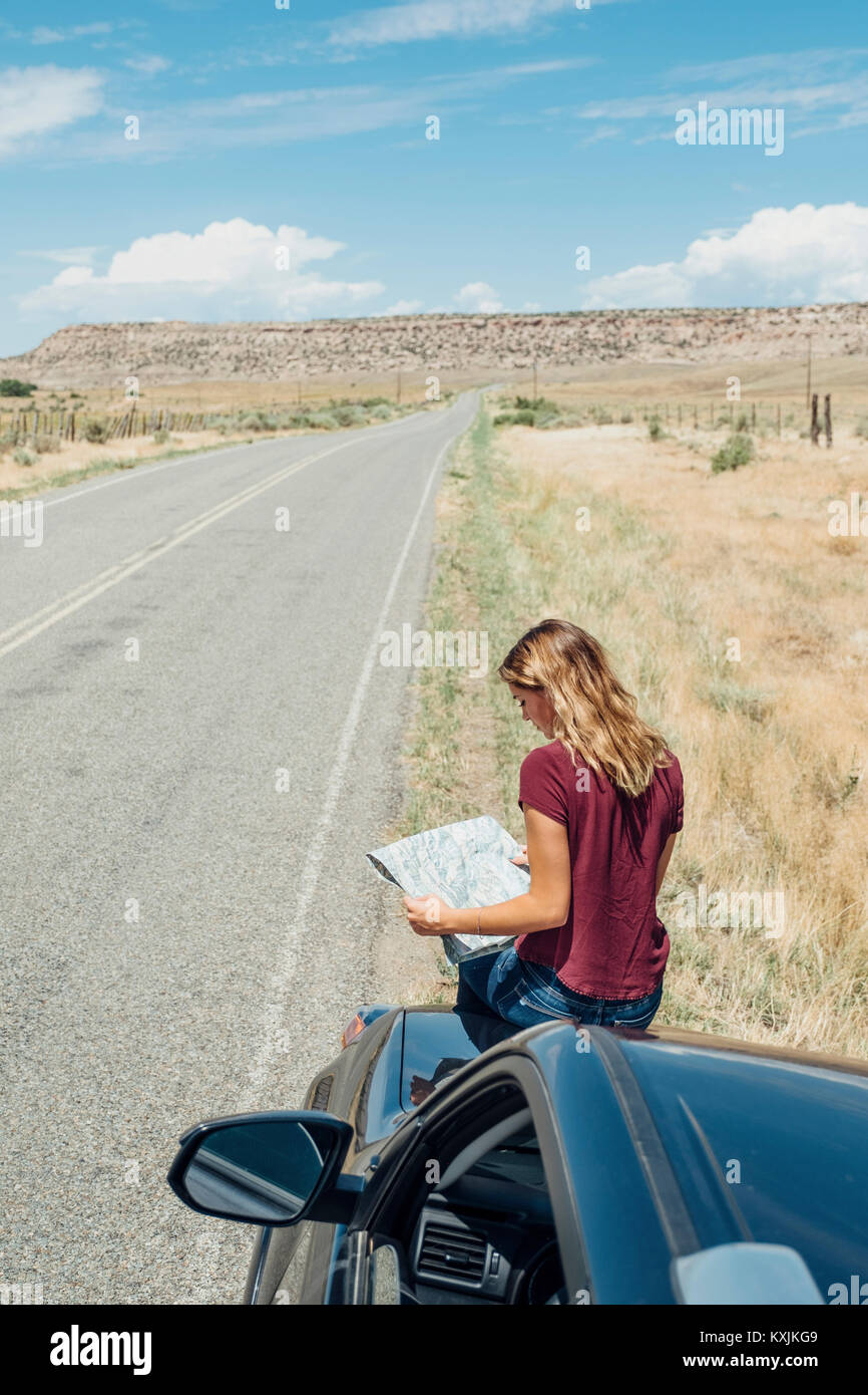 Woman sitting on car looking at map Banque D'Images