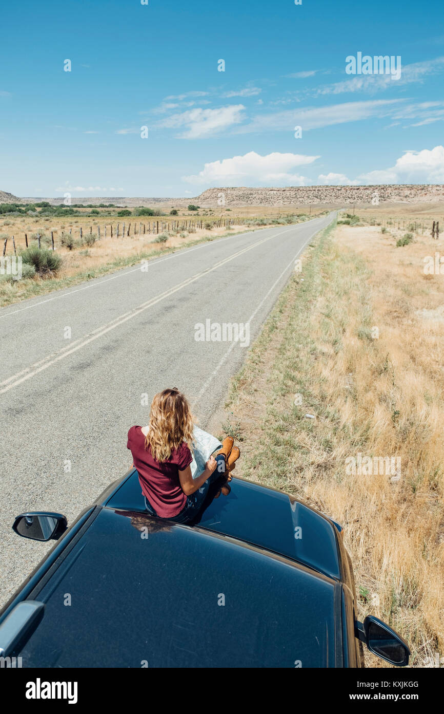 Woman sitting on car looking at map Banque D'Images