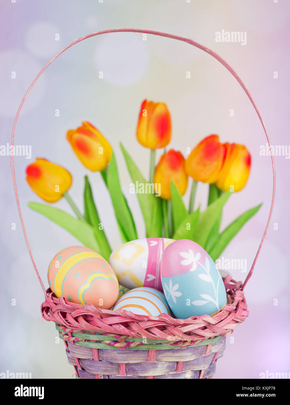 Les oeufs de Pâques colorés dans un panier avec des tulipes en arrière-plan Banque D'Images