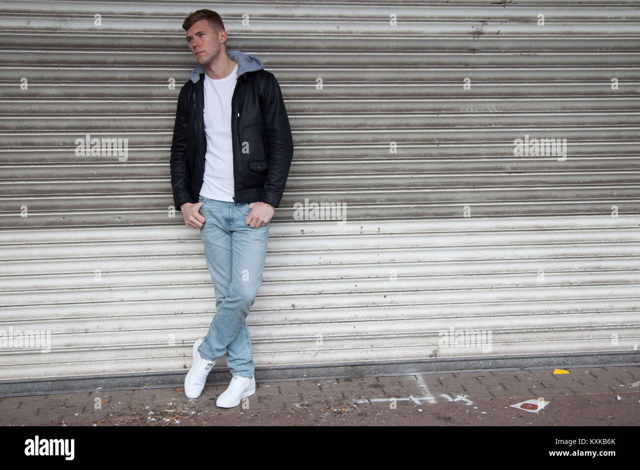 Bon à la blonde, modèle masculin s'appuyant sur volets boutique en centre commercial déserté Banque D'Images