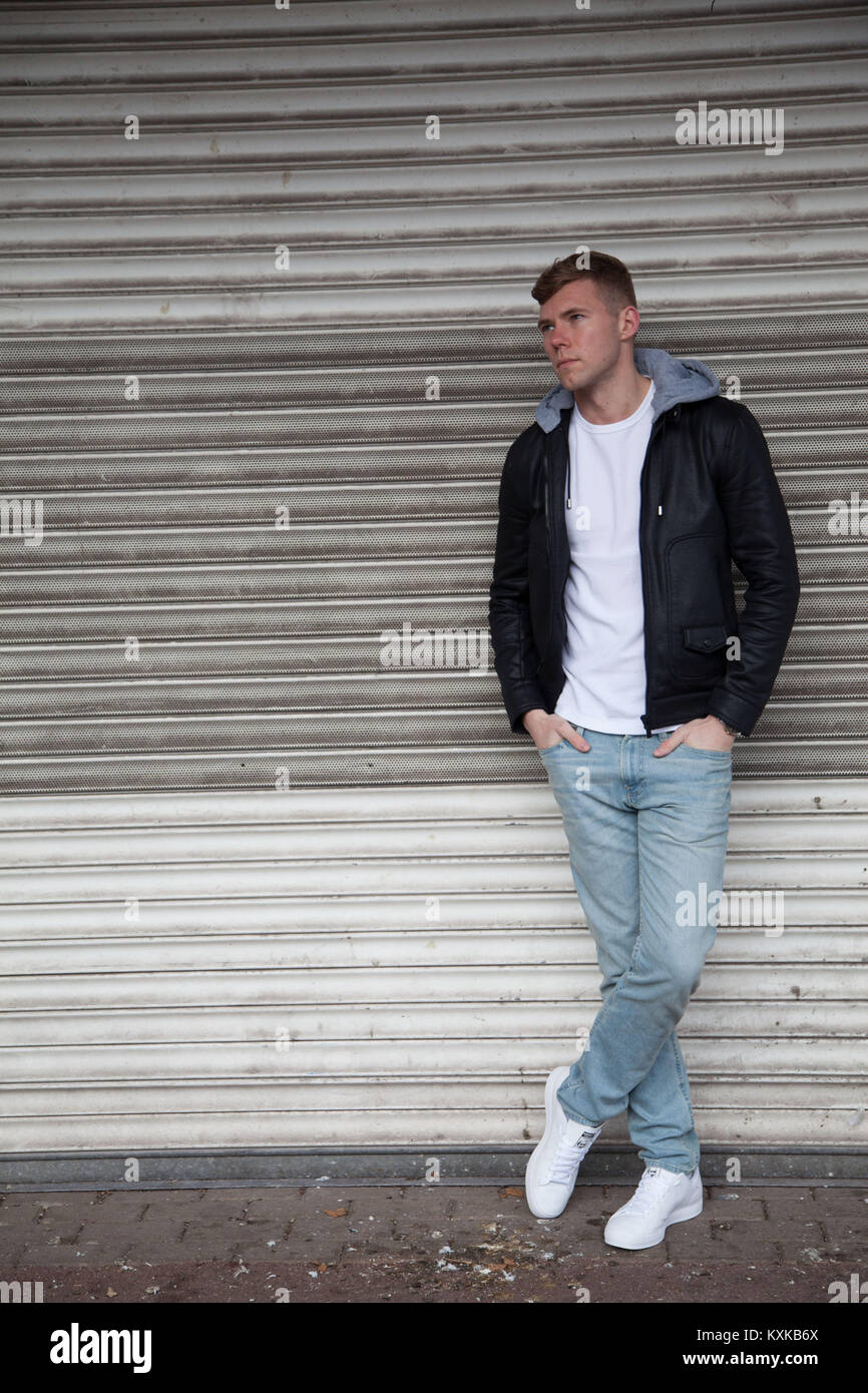 Bon à la blonde, modèle masculin s'appuyant sur volets boutique en centre commercial déserté Banque D'Images