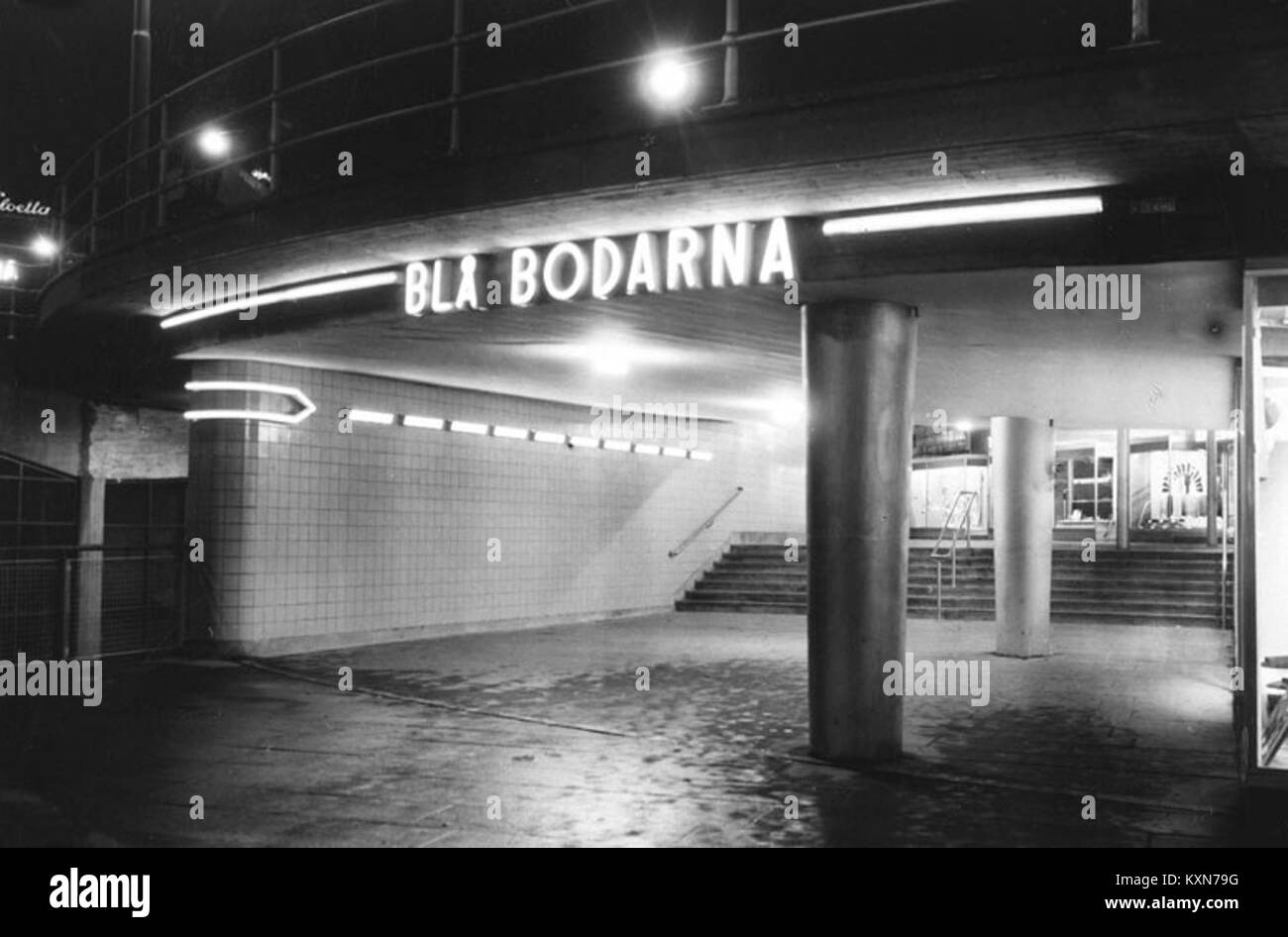 Cette photographie en noir et blanc de 1936 représente Blå Bodarna, un groupe de bâtiments en bois situés dans un paysage enneigé, avec des individus visibles au premier plan. L'image capture un moment dans le temps, mettant en valeur le style architectural et les conditions environnementales de l'époque. Banque D'Images