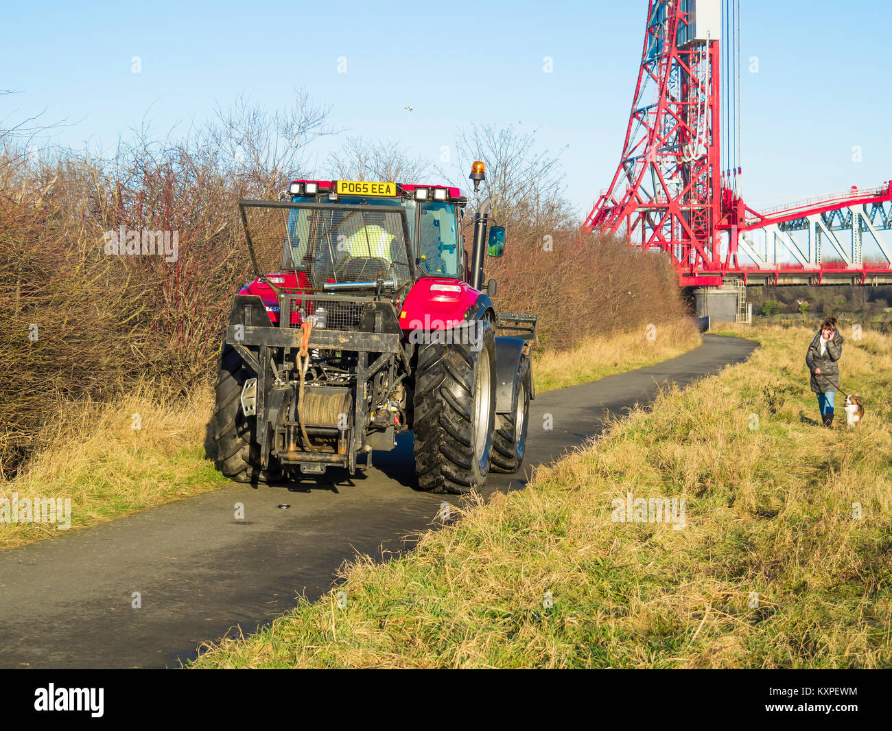 Un grand tracteur équipé d'un treuil rencontre une femme avec un chien sur le chemin Riverside Tees près du pont de Newport Banque D'Images