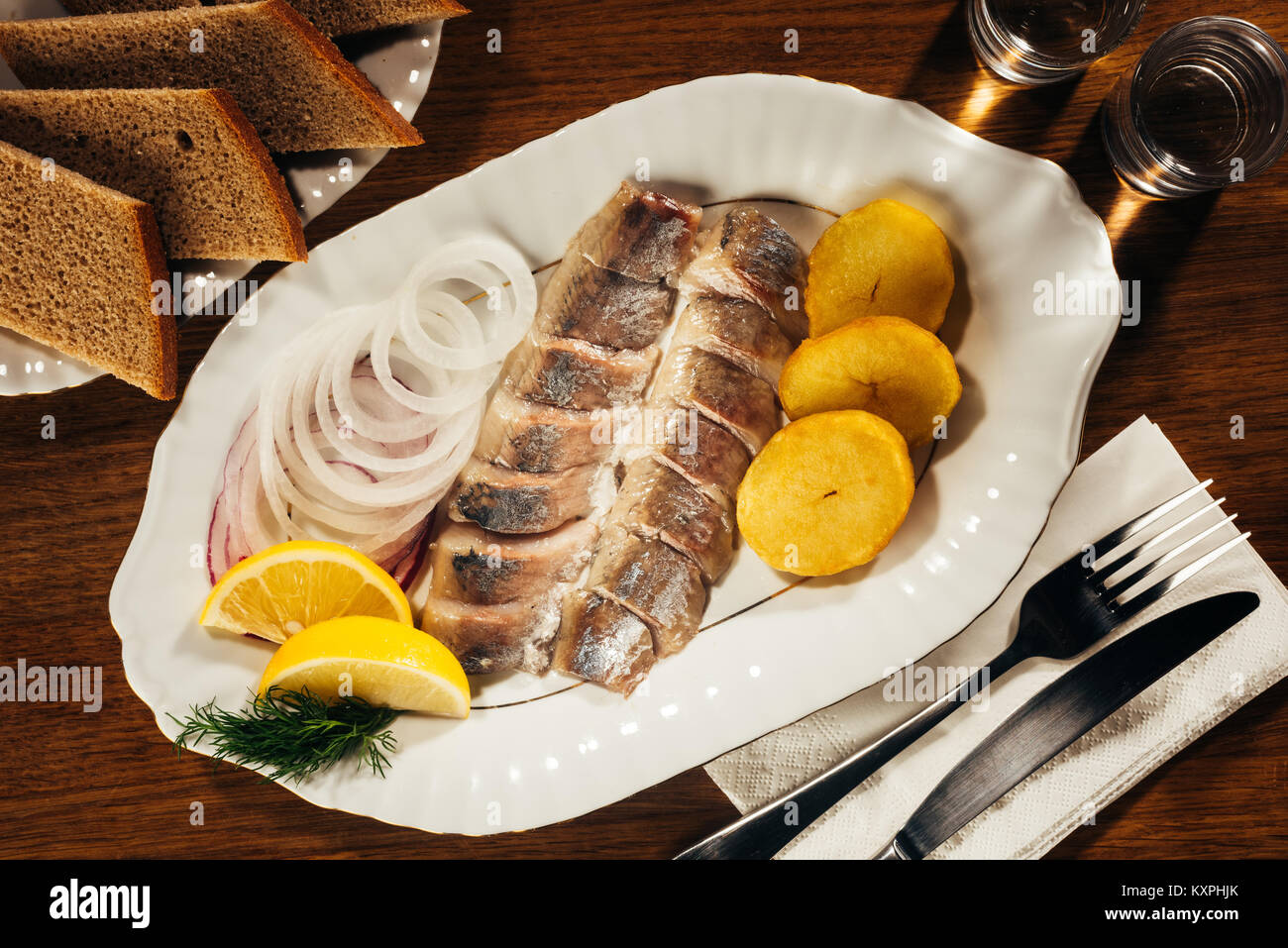 Tranches de poisson hareng portant sur la plaque avec l'oignon et les tranches d'orange sur le tableau avec la fourchette et le couteau à pain et serviette Banque D'Images