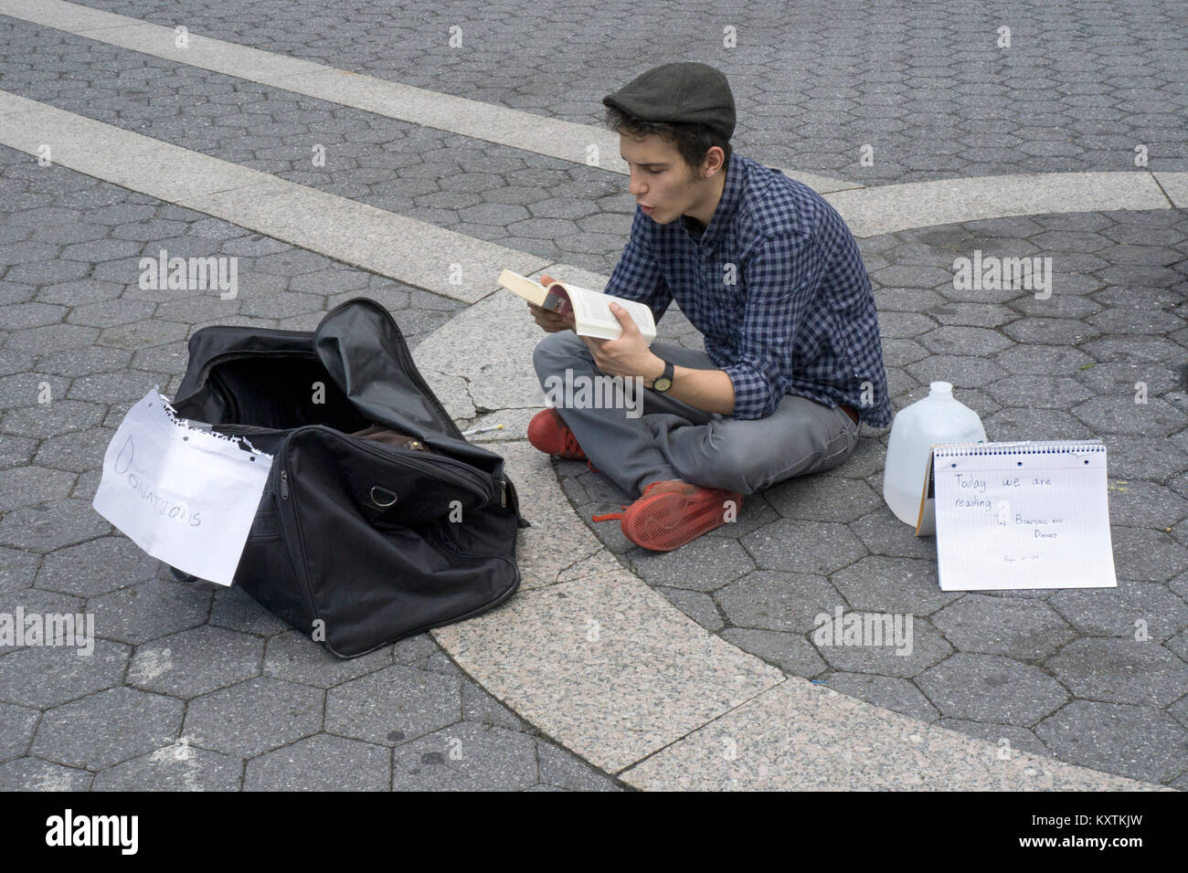 Un jeune homme la sollicitation de dons par la lecture à haute voix de F. Scott Fitzgerald's roman La Belle et les damnés. Dans la région de Union Square Park à Manhattan. Banque D'Images