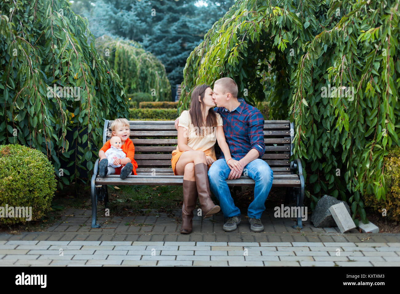 Papa et maman s'asseoir sur le banc et baiser. Fille est assise près de. Banque D'Images