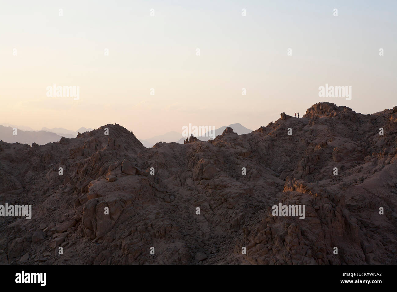 Deux personnes dans la distance debout au sommet d'une montagne dans la lumière du soir ayant une photo prise. Banque D'Images