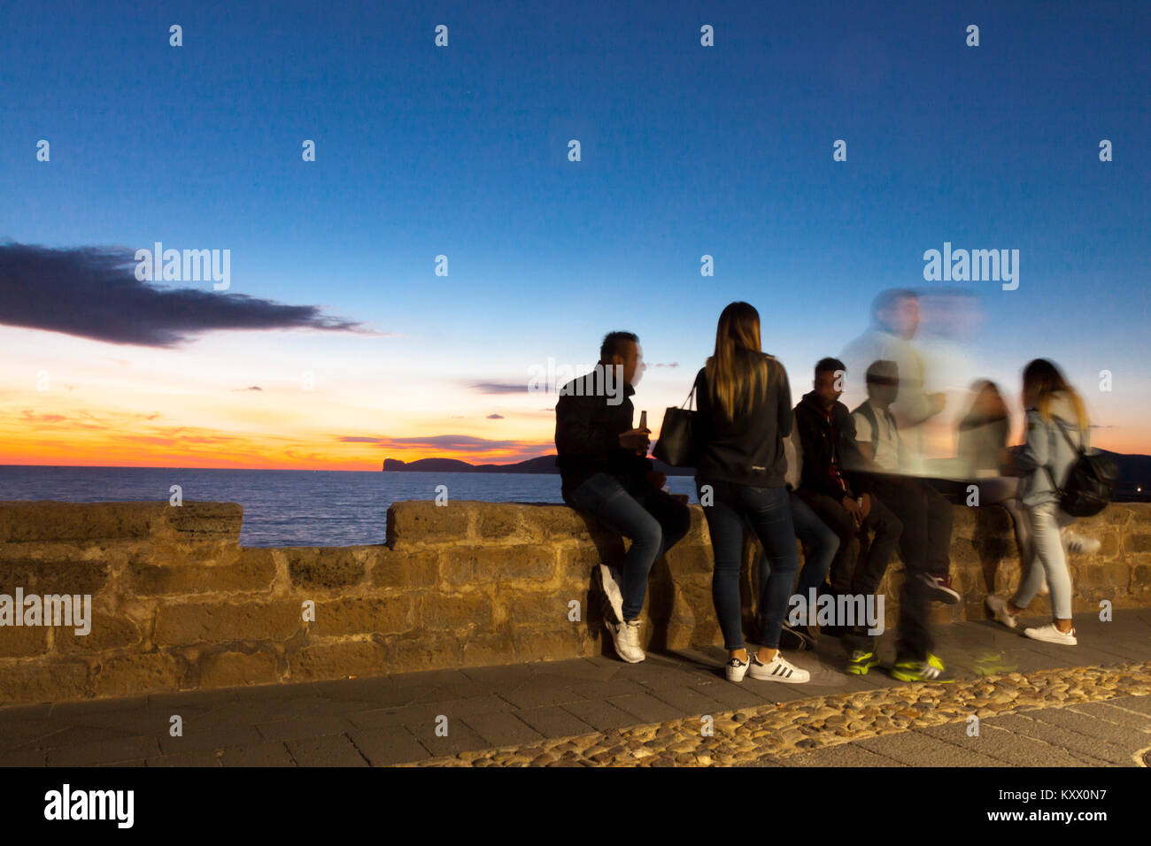 Les gars assis sur le mur de la ville et un cocktail ciel romantique au coucher du soleil. Alghero, Sardaigne. Italie Banque D'Images