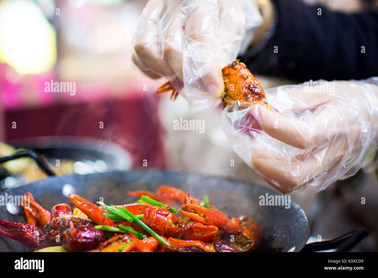 Les mains avec des gants en plastique en tenant les écrevisses des écrevisses épicée pot sur la table Banque D'Images