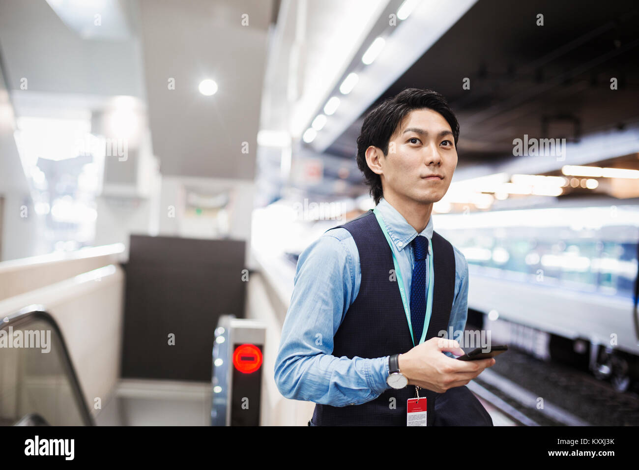 Businessman wearing blue shirt et gilet debout sur la plate-forme de la gare, holding mobile phone. Banque D'Images