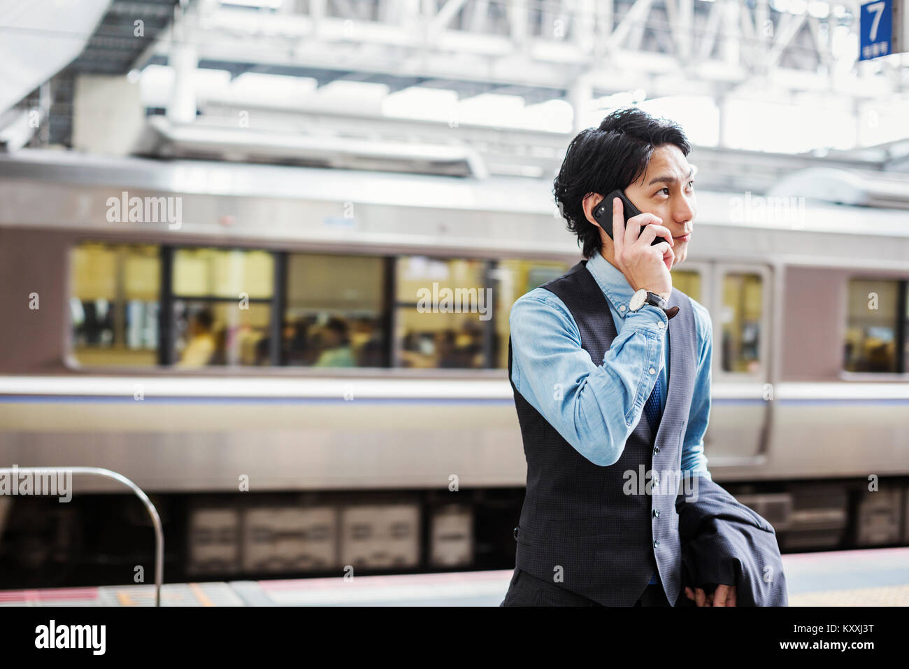 Businessman wearing blue shirt et gilet debout sur la plate-forme de la gare, talking on mobile phone. Banque D'Images