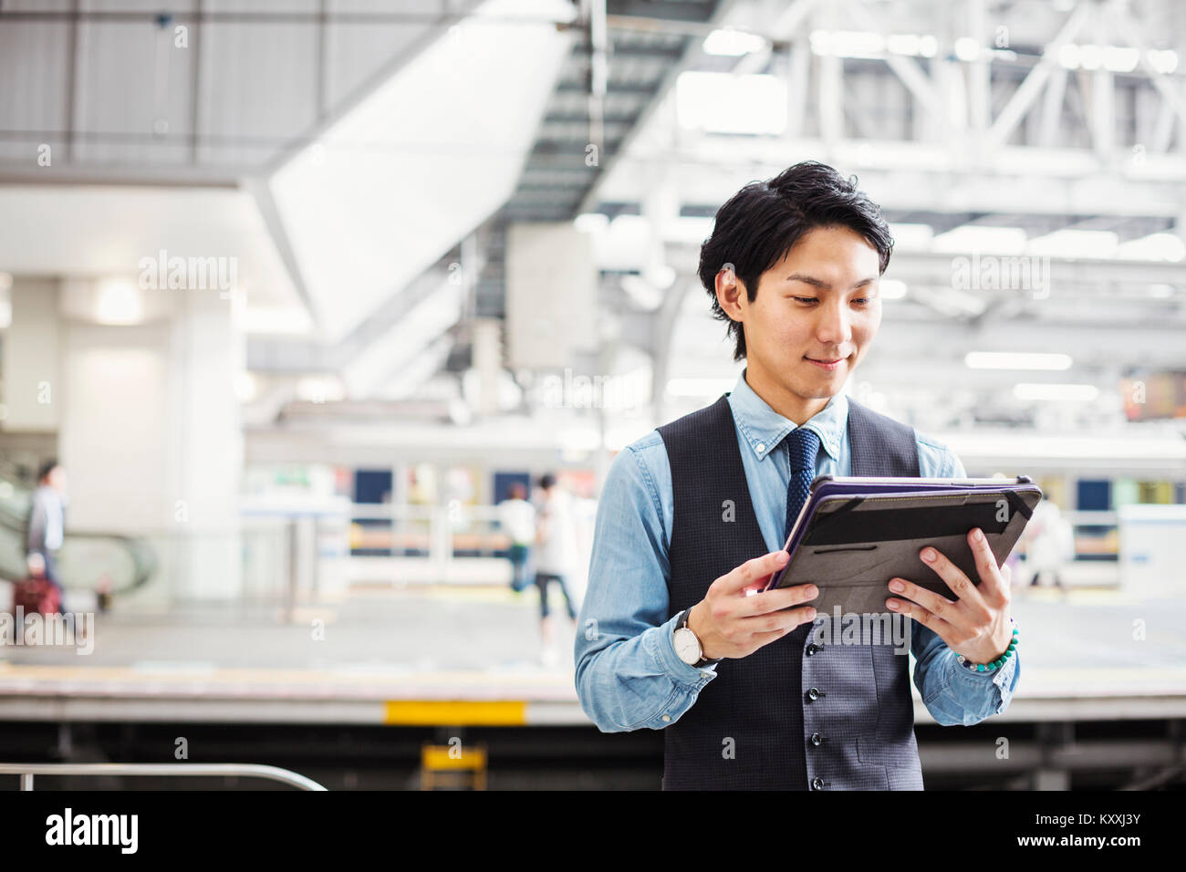 Businessman wearing blue shirt et gilet debout sur la plate-forme de la gare, holding digital tablet. Banque D'Images