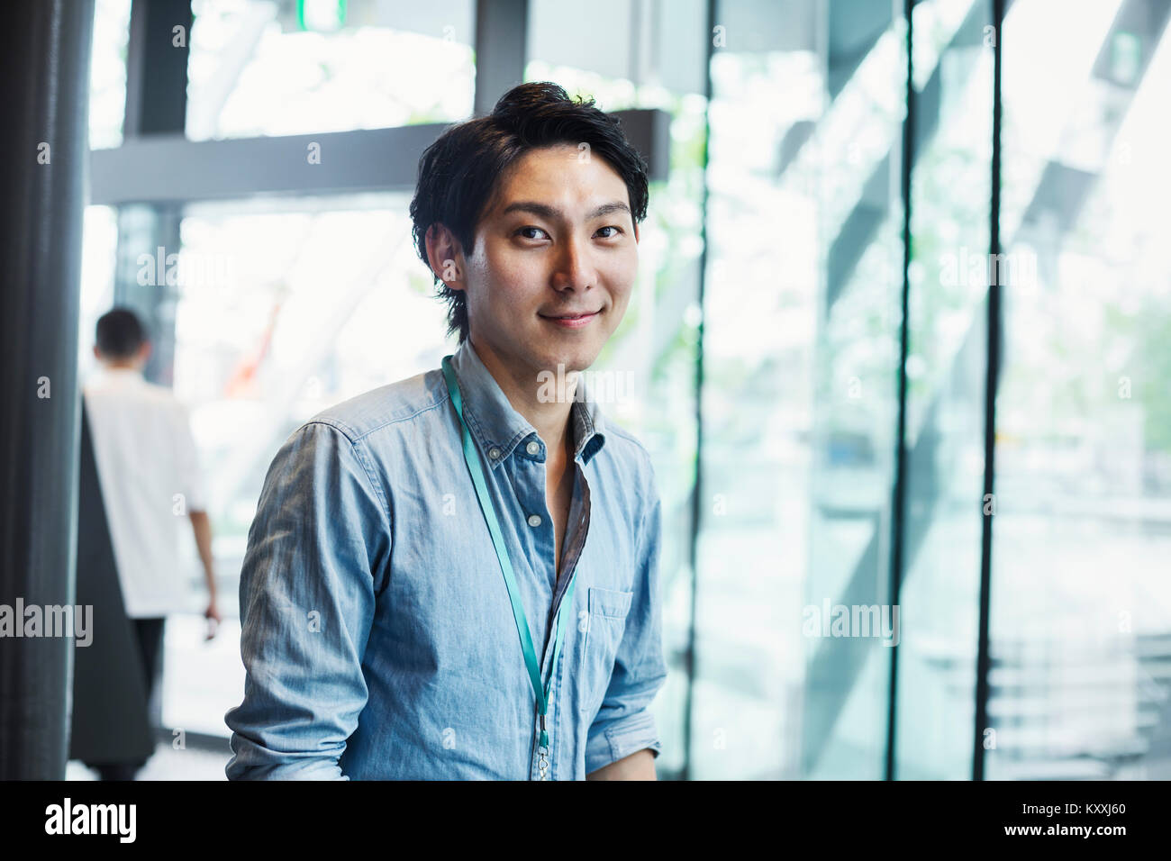 Businessman wearing blue shirt debout à l'intérieur par un mur de verre, looking at camera. Banque D'Images