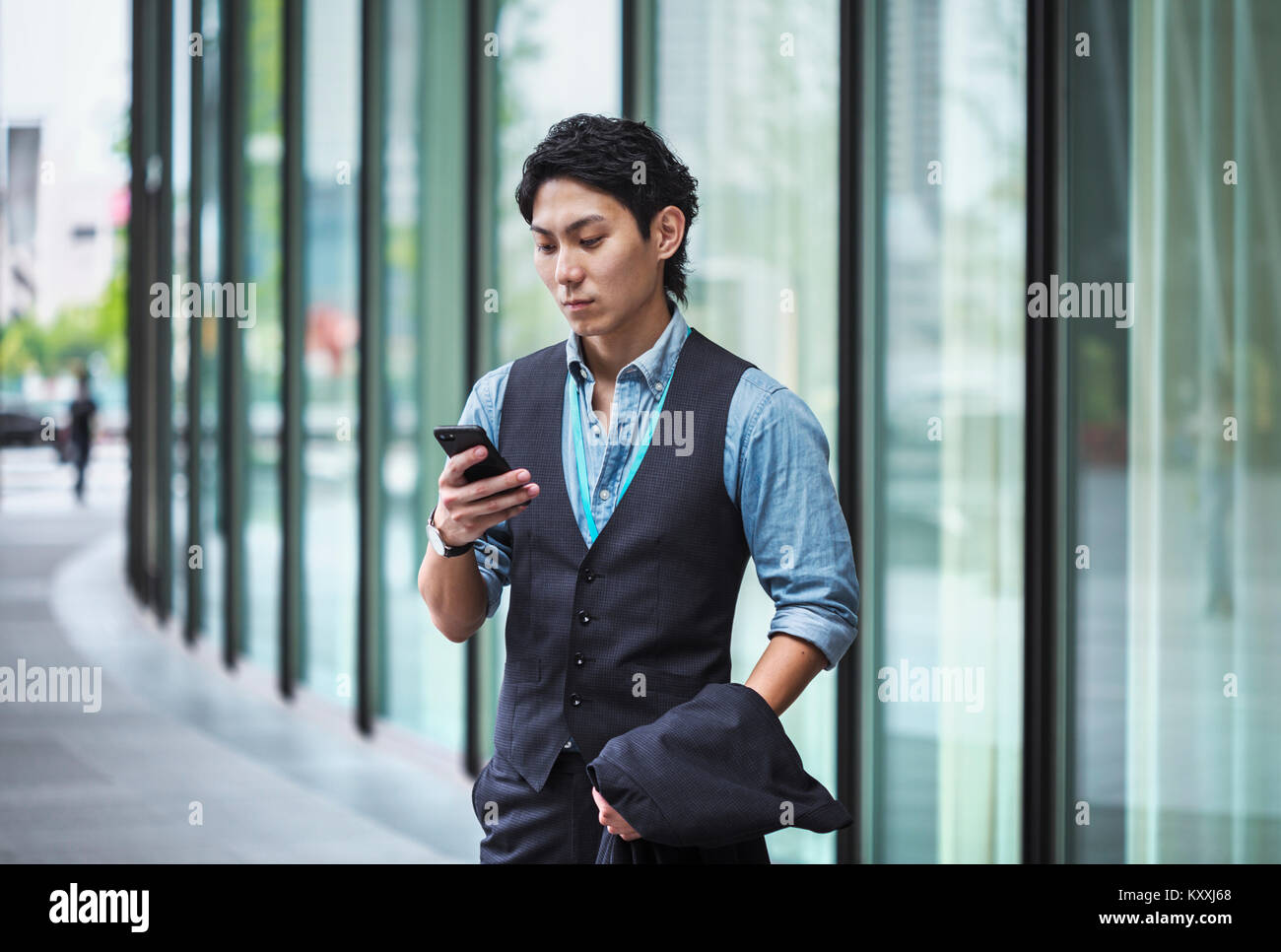 Businessman wearing blue shirt et gilet standing outdoors, holding mobile phone. Banque D'Images