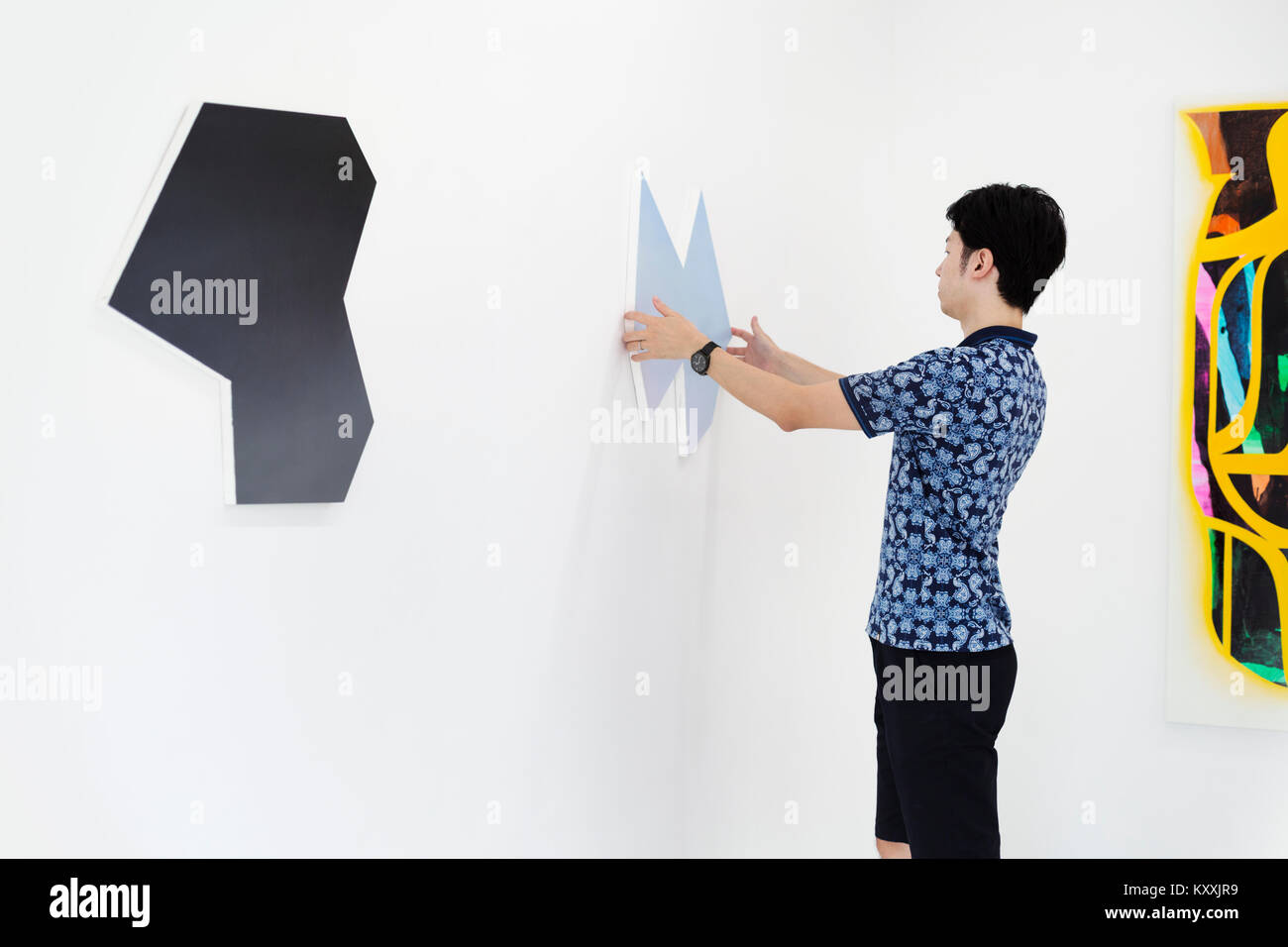 Vue de côté de l'homme avec les cheveux noirs courts wearing blue shirt debout dans la galerie d'art, la peinture moderne suspendue sur mur blanc. Banque D'Images