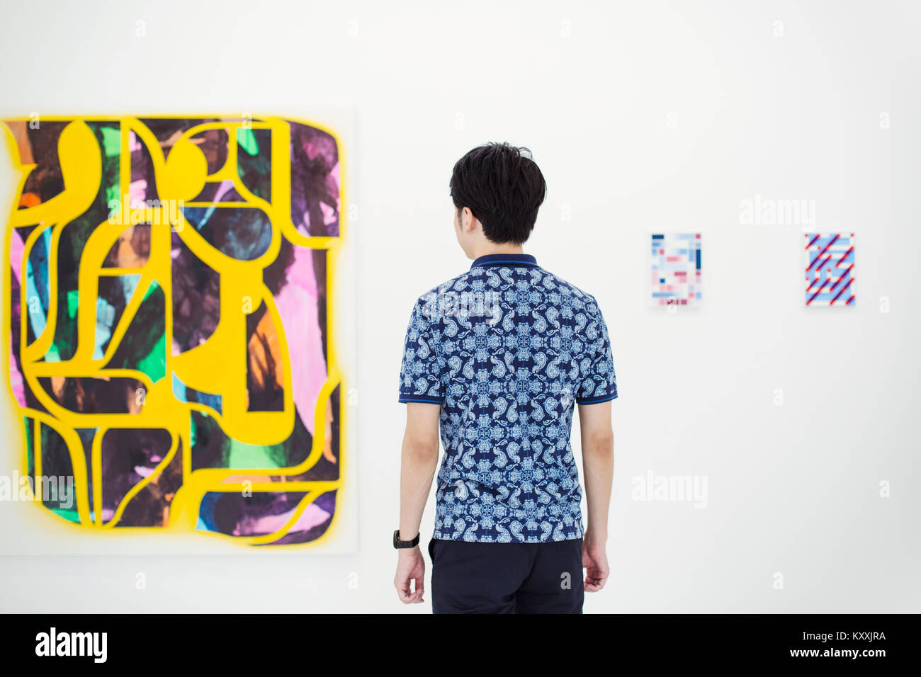 Vue arrière de l'homme avec les cheveux noirs courts wearing blue shirt debout dans une galerie d'art, à la peinture moderne au résumé. Banque D'Images
