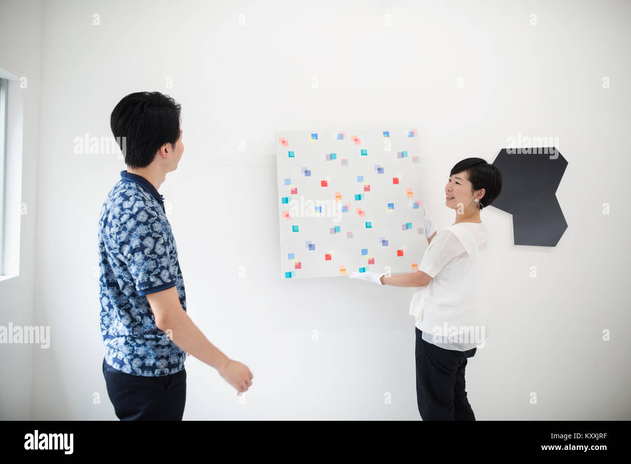 Man wearing blue shirt femme regarder accrocher la peinture moderne sur mur blanc dans l'art gallery. Banque D'Images