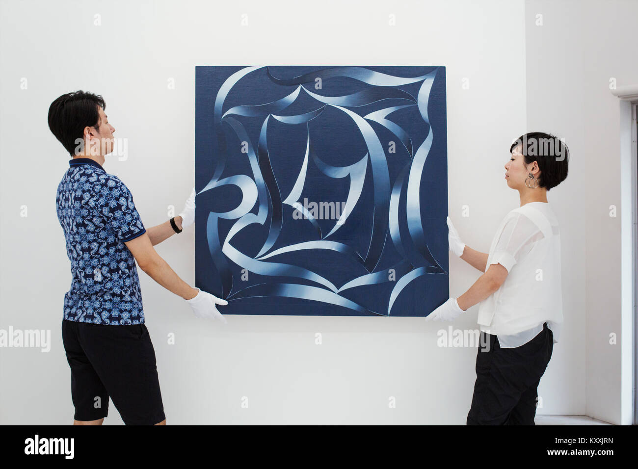 L'homme en chemise bleue et woman wearing white shirt hanging peinture moderne sur mur blanc dans l'art gallery. Banque D'Images