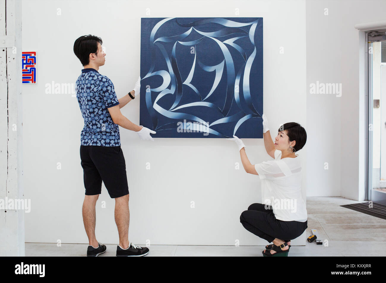 L'homme en chemise bleue et woman wearing white shirt hanging peinture moderne sur mur blanc dans l'art gallery. Banque D'Images