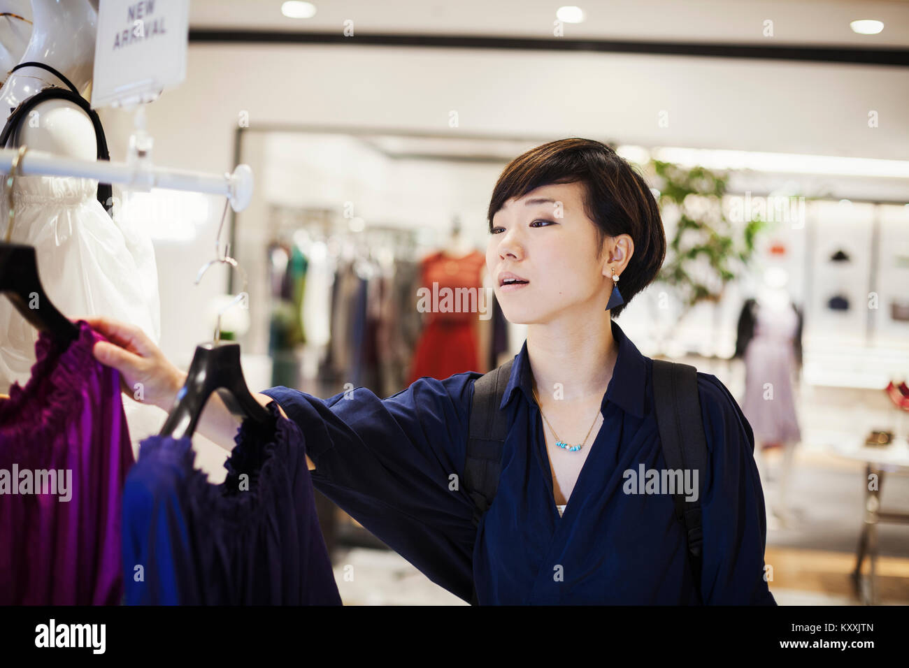 Femme aux cheveux noirs wearing blue shirt debout à l'intérieur, à la recherche à l'habillement dans un magasin. Banque D'Images
